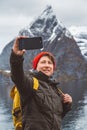 Portrait traveler man taking self-portrait a photo with a smartphone. Tourist in a yellow backpack standing on a background of a Royalty Free Stock Photo