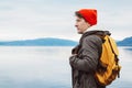 Portrait traveler man with a yellow backpack wearing a red hat on the shore on the background of mountain and lake