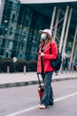 Portrait of a traveler woman in a mask walking with an orange suitcase near an airport. Young fashionable woman in a