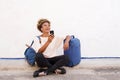 Traveling young woman sitting on sidewalk with suitcase and listening to music Royalty Free Stock Photo