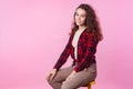 Portrait of trendy beautiful teenage girl sitting relaxed on chair and looking at camera with cute smile. pink background Royalty Free Stock Photo