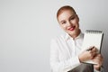 Portrait of trendy redhead woman posing in shirt holding empty notepad over white background. Royalty Free Stock Photo