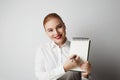 Portrait of trendy redhead woman posing in shirt holding empty notepad over white background. Royalty Free Stock Photo