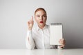 Portrait of trendy redhead woman posing in shirt holding empty notepad over white background. Royalty Free Stock Photo