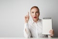 Portrait of trendy redhead woman posing in shirt holding empty notepad over white background. Royalty Free Stock Photo