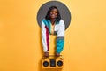 Portrait of trendy stylish woman in retro jacket and eyewear holding boombox looking at camera isolated on yellow background. Copy