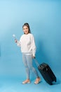 Portrait of trendy young girl standing with suitcase and holding passport with tickets, over blue background Royalty Free Stock Photo