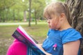 A portrait of trisomie 21 child girl outside having fun on a park reading book