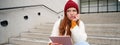 Portrait of troubled redhead girl, college student with thoughtful face, sits on street stairs, holds digital tablet