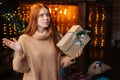 Portrait of troubled redhead young woman holding in hand beautiful gift box with Christmas present. Royalty Free Stock Photo