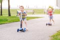 Two active little children friends girl and boy riding scooters on road in park outdoors Royalty Free Stock Photo