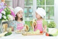 Portrait of two adorable little girls in aprons eating bananas at kitchen