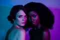 Portrait of two affectionate tempting women bonding flirty isolated over vivid violet purple blue neon color background