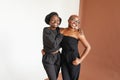 Portrait of two african american young friend in black costumes smiling and hugging in studio on white and brown background Royalty Free Stock Photo