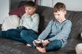 Portrait of two angry indignant teenage boys sitting on sofa at home, holding joystick, playing videogames, losing game.