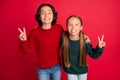 Portrait of two attractive cheerful friends showing v-sign hugging having fun isolated over bright red color background Royalty Free Stock Photo