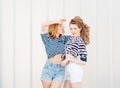 Portrait of two beautiful fashionable girlfriends in denim shorts and striped t-shirt posing nex to the glass wall. Girl showing Royalty Free Stock Photo