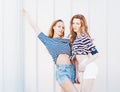 Portrait of two beautiful fashionable girlfriends in denim shorts and striped t-shirt posing nex to the glass wall. Outdoors. War