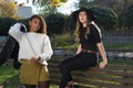 Portrait of two beautiful mexican generation z girls. A girl in a black hat sits on the back of a bench, next to a girl with curly