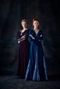 Portrait of two beautiful women in image of queen and princess isolated over dark background. Royal family Royalty Free Stock Photo