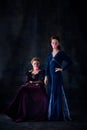 Portrait of two beautiful women in image of queen and princess posing with bubblegum isolated over dark background Royalty Free Stock Photo