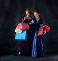 Portrait of two beautiful women in image of queen and princess with shopping bags isolated over dark background Royalty Free Stock Photo