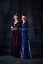 Portrait of two beautiful women in image of queen and princess in stylish sunglasses isolated over dark background Royalty Free Stock Photo