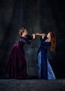 Portrait of two beautiful women in image of queens fighting for giant sandwich isolated over dark background Royalty Free Stock Photo