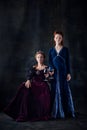 Portrait of two beautiful women in image of queens isolated over dark background. Royal family legacy Royalty Free Stock Photo