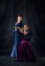 Portrait of two beautiful women in image of royal persons isolated over dark background. Queen eating big sandwich Royalty Free Stock Photo