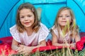 Portrait of two blonde and pretty sisters lying down in a blue camping tent Royalty Free Stock Photo