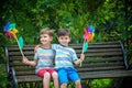 Portrait of two boys, sibling brothers and best friends smiling. Kids sitting on bench play together with pinwheel. Outdoors