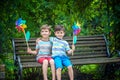 Portrait of two boys, sibling brothers and best friends smiling. Kids sitting on bench play together with pinwheel. Outdoors