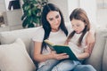 Portrait of two brown haired people lovely caring mother teach her daughter read book girl concentrated sit divan couch Royalty Free Stock Photo