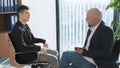 Portrait of two businessman sitting and chatting with office background. Casual looking men in suits discussing