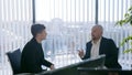 Portrait of two businessman sitting and chatting with office background. Casual looking men in suits discussing