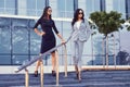 Portrait of two businesswomen dressed in a stylish formal clothes, standing on steps posing against a background of a Royalty Free Stock Photo