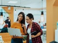 Portrait of two businesswomen talking to each other while standing in a modern business office with their colleagues Royalty Free Stock Photo