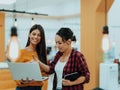 Portrait of two businesswomen talking to each other while standing in a modern business office with their colleagues Royalty Free Stock Photo