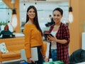 Portrait of two businesswomen talking to each other while standing in a modern business office with their colleagues Royalty Free Stock Photo