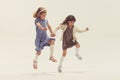 Portrait of two cheerful happy girls, children in beautiful dresses playing together, jumping isolated over grey studio Royalty Free Stock Photo