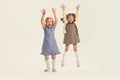 Portrait of two cheerful little girls, children jumping, playing isolated over grey studio background Royalty Free Stock Photo