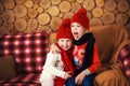 Portrait of two children, boy and girl, brother and sister, siblings in red hats and scarves sitting on sofa in wooden room. Curly Royalty Free Stock Photo