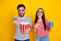 Portrait of two crazy cheerful people watch movie 3d glasses hold popcorn soda drink finger point you isolated on yellow Royalty Free Stock Photo