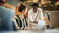 Portrait of Two Creative Young Colleagues Consulting Eachother Using Laptop in Modern Office. Black Royalty Free Stock Photo