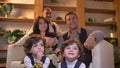 Portrait of two cute arabic curly-headed twins sitting on floor in living room smilingly watching TV with their family