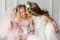 Portrait of two cute and beauty little girl - sisters in wreaths of fresh flowers have fun and smile in a bright studio. Close-up Royalty Free Stock Photo