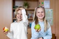 Portrait of two cute caucasian young blond little classmate friend kids eating apple in classroom at lunch time pause