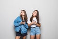 Portrait of two cute mixed race women using cell phones isolated over gray background Royalty Free Stock Photo