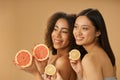Portrait of two cute mixed race young women smiling aside, holding grapefruit and lemon cut in half while posing